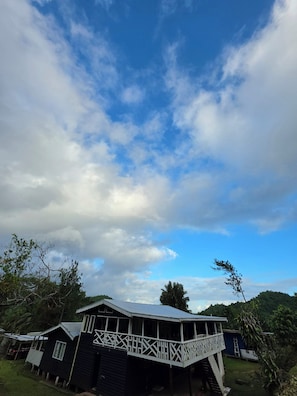 A two-story building with a balcony, surrounded by trees and under a partly cloudy sky.