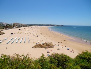 A beach with rows of sunbeds, a rocky outcrop, and a clear sky. - Studio Flat Paraíso Sol da Rocha (Portimão)