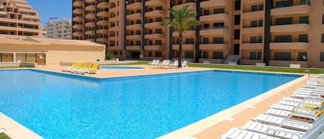 A swimming pool with lounge chairs, surrounded by multi-story buildings.