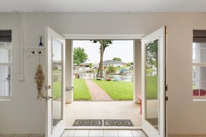 Eine offene Tür, die zu einem Garten mit einem Weg, einem Baum und Blick auf eine Wohngegend führt.