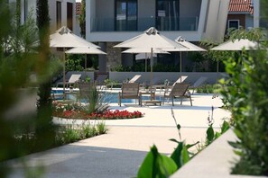 Ein Poolbereich mit Liegestühlen und Sonnenschirmen, umgeben von Grünflächen und einem modernen Gebäude.