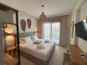 Ein Hotelzimmer mit Bett, Schreibtisch, Stuhl, Fernseher und einem großen Fenster mit Vorhängen.
