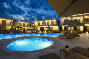 A swimming pool with lounge chairs and umbrellas, surrounded by modern buildings with large windows. - Darion Residence A5 - Apartament Steps from the Sea (Nikiti)