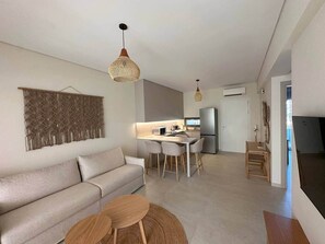 Ein modernes Wohnzimmer mit Sofa, Esstisch mit Stühlen und einer Küchenzeile im Hintergrund.
