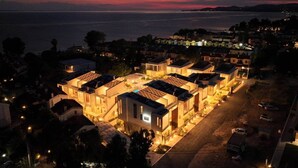 Zona residencial con varias casas, una piscina y vista al mar al atardecer.