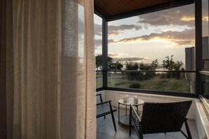 A balcony with a view of a sunset, a table with chairs, and a window with curtains. - Villas Thallo № 3 (Neos Marmaras)