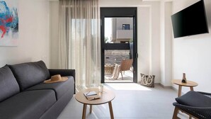 Ein modernes Wohnzimmer mit einer Couch, einem kleinen runden Tisch, einem Sessel, einem Fernseher und einer Glasschiebetür, die zu einem Außenbereich führt.