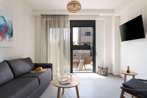A modern living room with a sofa, a small round table, a chair, a TV, and a sliding glass door leading to an outdoor area. - Villas Thallo № 4 (Neos Marmaras)