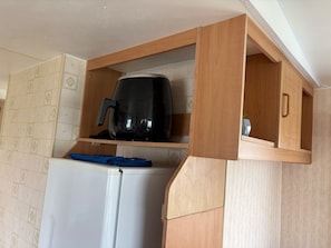 A compact kitchen with a built-in coffee maker, a white refrigerator, and wooden cabinetry.