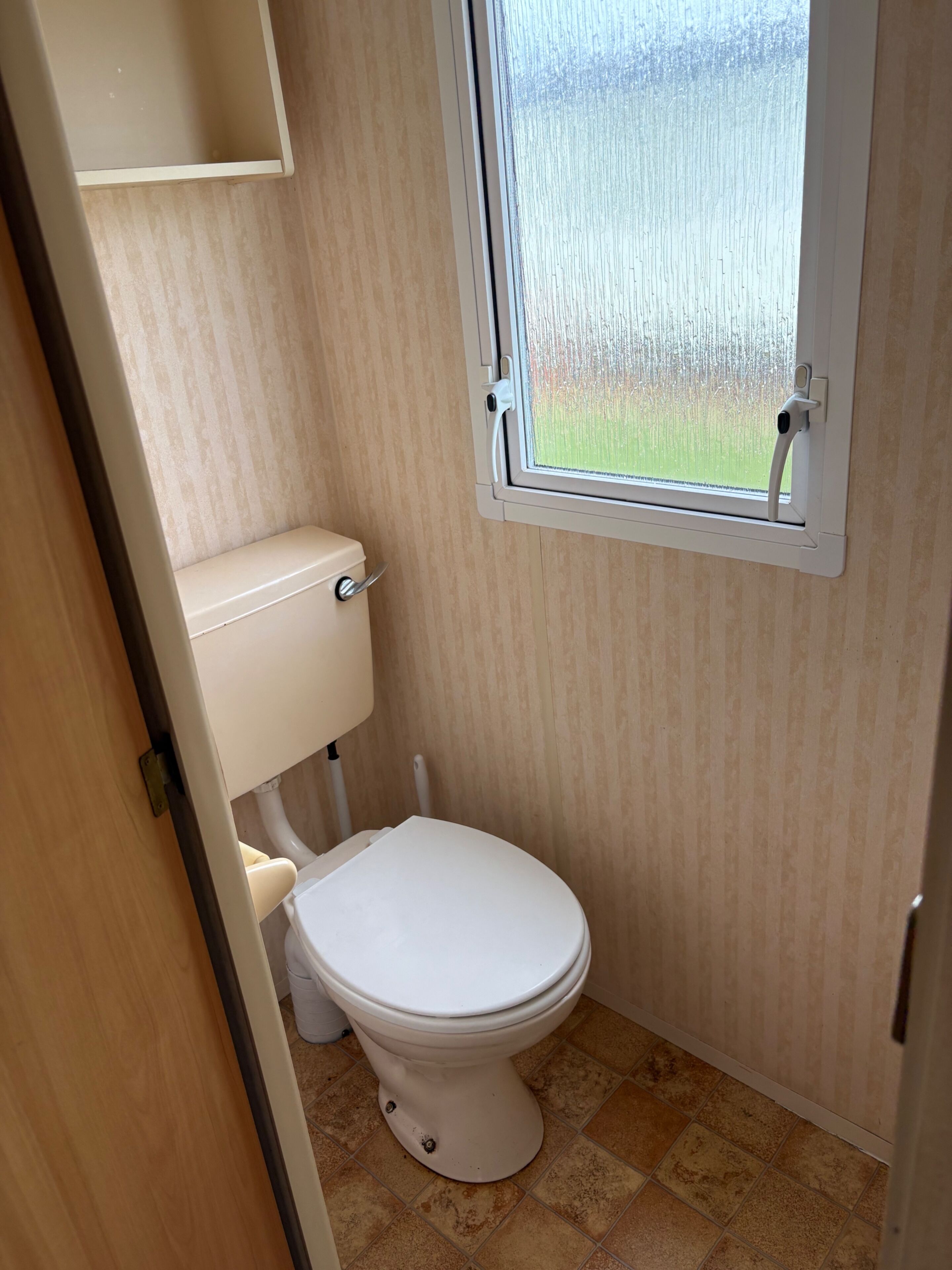 Un bagno piccolo e funzionale, con il water, una finestra e una parete in legno.