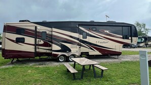 A large RV with a covered living area, a dining table, and a picnic table. - Cardinal Camper Getaway at Eddy's Place-Sleeps 8 (Moravia)