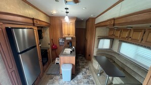 A compact kitchen with wooden cabinets, a stainless steel refrigerator, a sink, and a window with blinds. - Cardinal Camper Getaway at Eddy's Place-Sleeps 8 (Moravia)