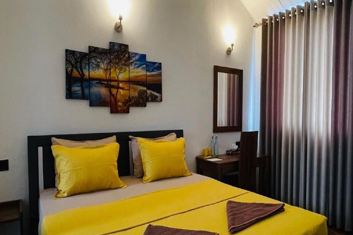 Habitación de hotel con cama, mesita de noche, escritorio, silla, un cuadro en la pared y cortinas.
