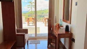 A room with a wooden desk, a chair, a hanging coat rack, and a large sliding glass door leading to an outdoor area with a table and chairs. - Sun Dove Suit - Kandy (Kandy)