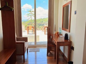 A room with a wooden desk, a chair, a hanging coat rack, and a large sliding glass door leading to an outdoor area with a table and chairs. - Sun Dove Suit - Kandy (Kandy)