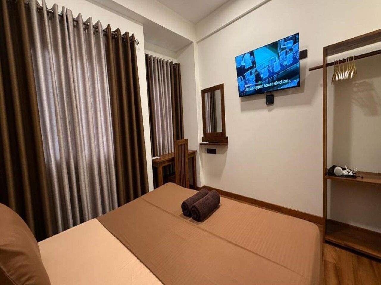 A hotel room with a bed, a television mounted on the wall, a mirror, and a wardrobe.