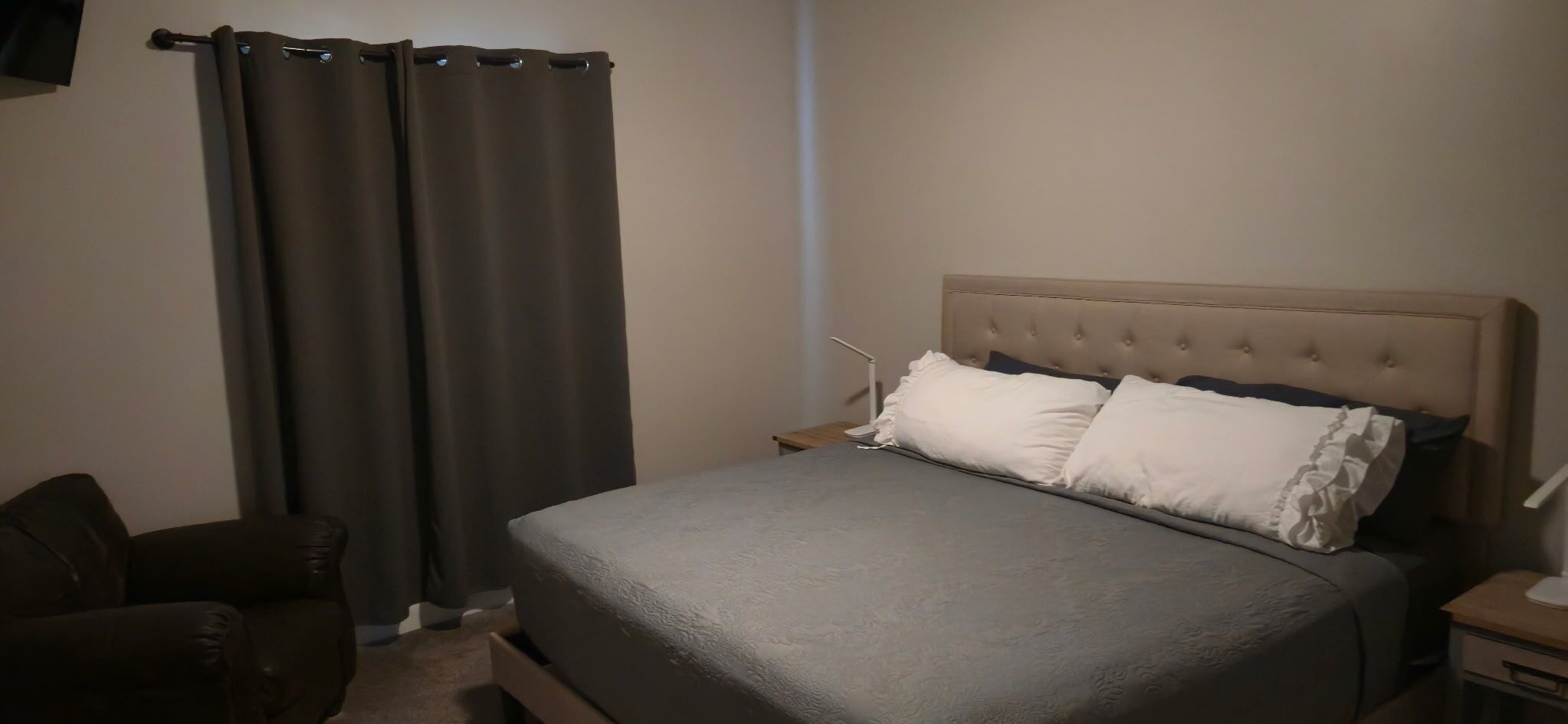 Une chambre à coucher avec un lit, une chaise, une table de chevet et une lampe.
