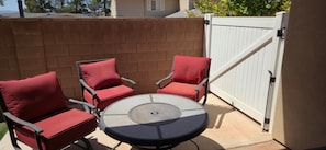 A patio with a round table and four chairs, a brick wall, and a white gate.