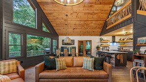 Een gezellig cabin interieur met een leren bank, houten plafond en grote ramen met uitzicht op een bos.