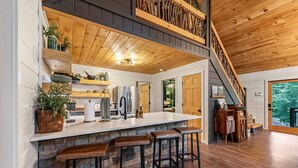 Een keuken met een centraal eiland, barstoelen, een houten plafond en een trap.