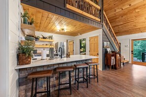 Eine Küche mit Kochinsel, Barhocker, Holzboden und einer Treppe.