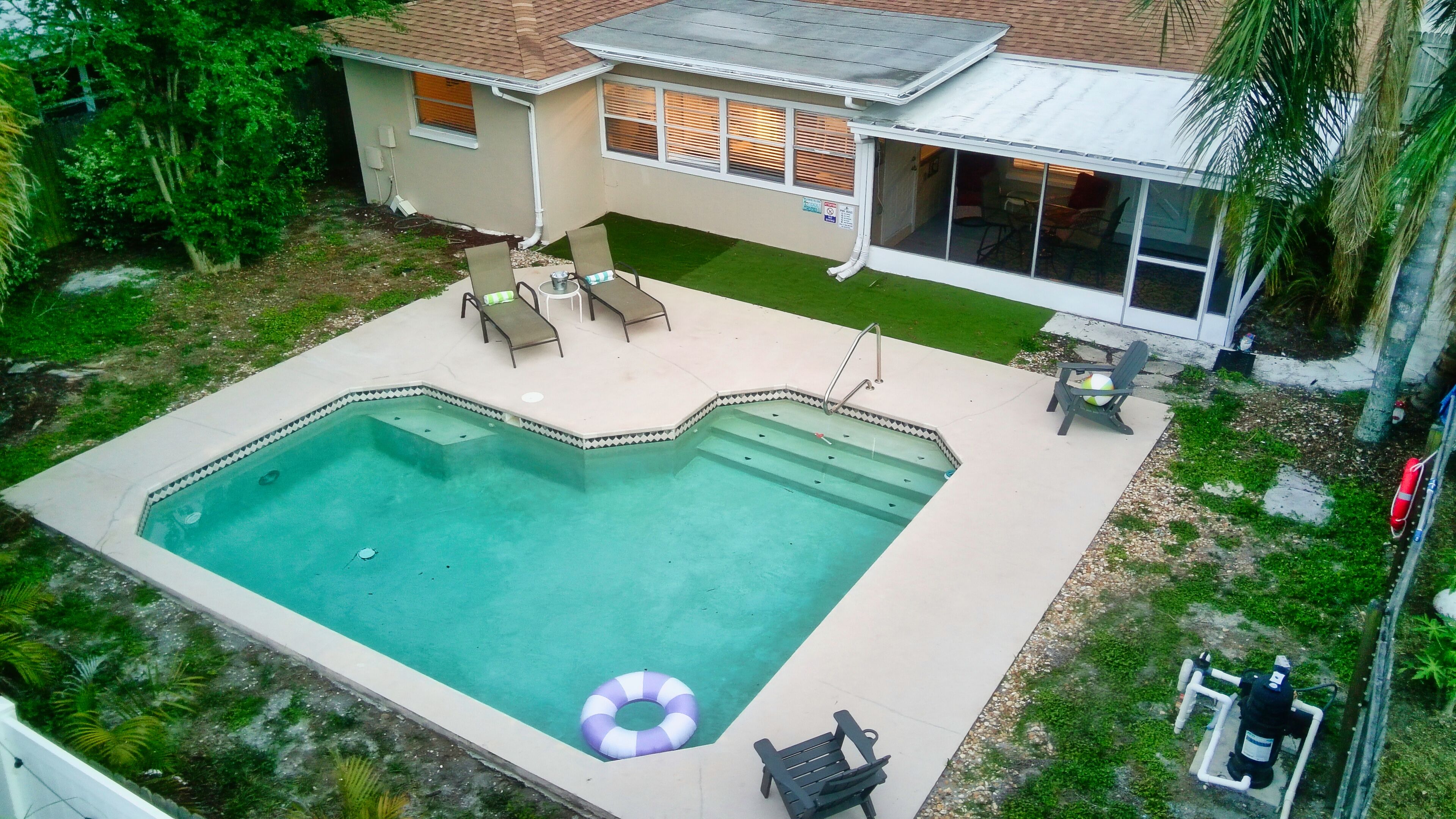 Une piscine résidentielle avec une terrasse carrelée, une chaise longue et un petit flotteur gonflable.