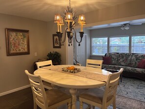 A dining area with a round table, chairs, a chandelier, a sofa, and a window with blinds. - Relaxed Clearwater Family Retreat with Private Pool and Patio (Clearwater)