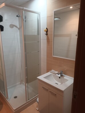 A bathroom with a glass-enclosed shower, a sink with a mirror above it, and a cabinet below.