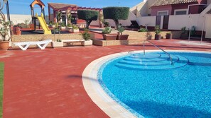 A swimming pool with a slide, surrounded by potted plants and a red deck. - Spain, Murcia region, family home, close to the sea, community pool. (Mazarrón)