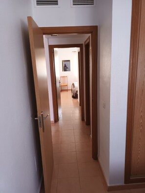 A hallway with a wooden door, a chair, and a bed in the distance.