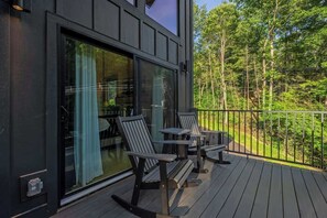 Une terrasse avec des fauteuils Adirondack et une table, donnant sur une zone boisée.