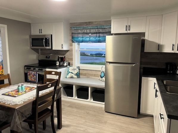 A compact kitchen with a microwave, stove, refrigerator, and a window with a view.