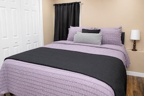 Un dormitorio con cama, mesita de noche, lámpara y puerta.