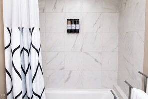A bathroom with a shower area, a bathtub, and a set of toiletries on the wall.