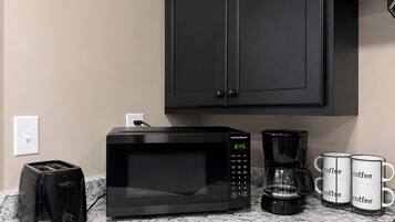 Eine Küche mit einer schwarzen Mikrowelle, einer Kaffeemaschine und vier Kaffeetassen auf der Arbeitsfläche.
