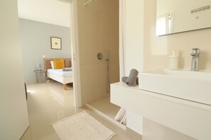 Un baño moderno con ducha, lavamanos y una cama al fondo.