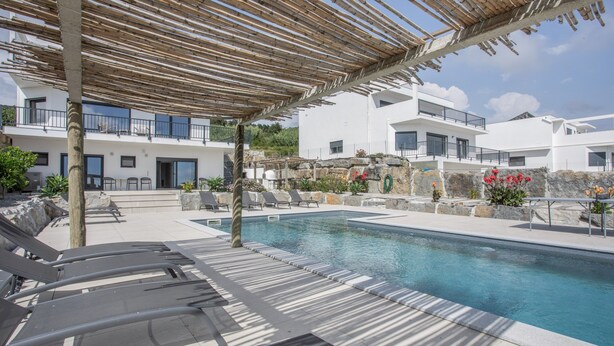 Et poolområde med liggestole, et pergola-område og udsigt til moderne bygninger.