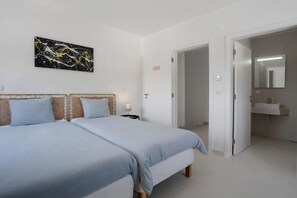 Et hotelværelse med to senge, et natbord, et ophængt kunstværk og en dør der står åben ind til et badeværelse.