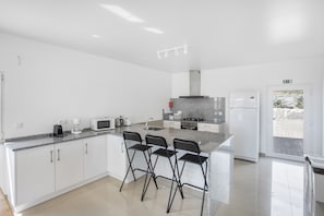 A modern kitchen with white cabinets, a granite countertop, a gas stove, a microwave, and a refrigerator. There are three black bar stools at the island. - 'Jade' Room with Shared Pool, Shared Terrace and Wi-Fi (Lourinhã)
