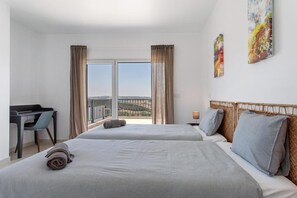 Habitación de hotel con dos camas, un escritorio, una silla y un balcón con vistas.