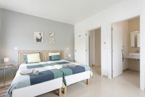 Ein Schlafzimmer mit Bett, Nachttischen, einer Tür und einem Badezimmer mit Spiegel und Waschbecken.