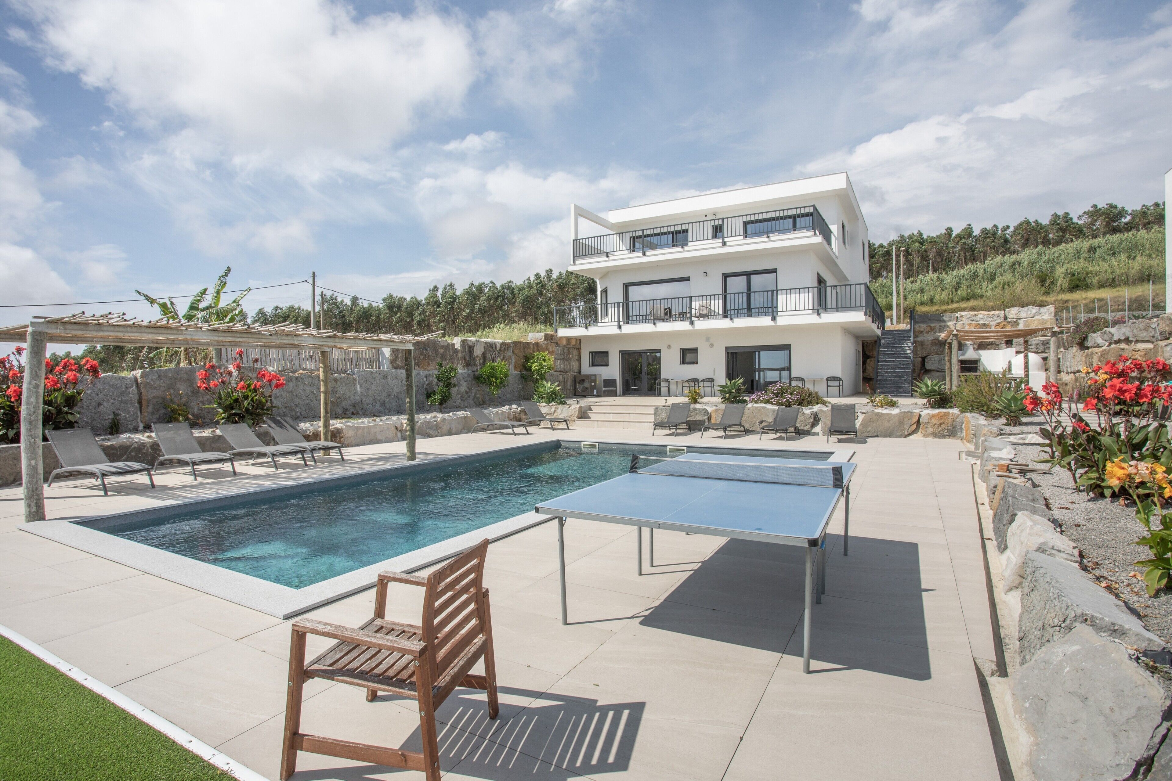 Una casa moderna de dos pisos con piscina, mobiliario exterior y mesa de ping pong.
