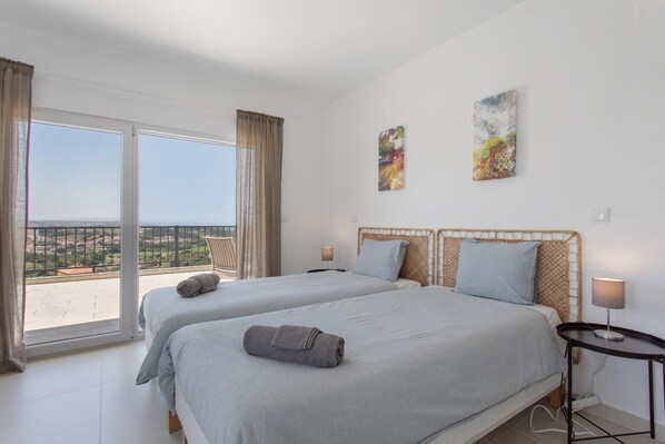 Habitación de hotel con dos camas, un balcón con vistas y dos cuadros abstractos en la pared.