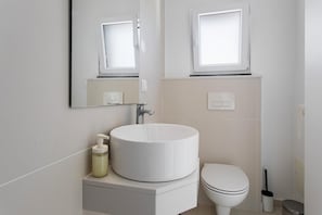Et moderne badeværelse med en rund vask, toilet, spejl og et vindue.