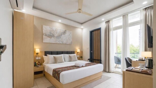 Habitación de hotel con cama, mesitas de noche, escritorio, silla, ventilador de techo, ventana con cortinas y un cuadro en la pared.