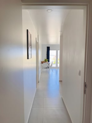 Un pasillo con paredes blancas, una luz en el techo y una puerta que da a una habitación con una mesa y sillas.