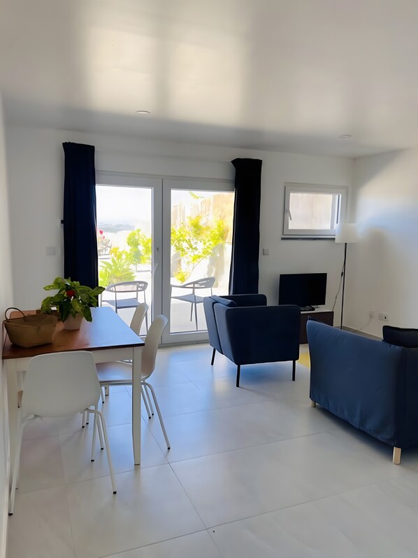 Ein modernes Wohnzimmer mit Essbereich, einer Couch, einem Fernseher und einem Balkon mit Blick.