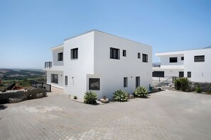 Un edificio moderno de dos pisos con techo plano, ventanas amplias y un patio empedrado.
