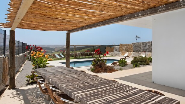 Ein überdachter Außenbereich mit Pool, Liegestühlen und Blick auf die Landschaft.