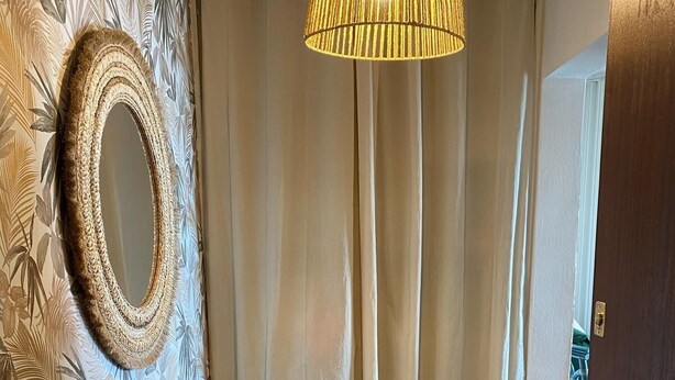 Ein Zimmer mit einer gemusterten Wand, einem runden Spiegel, einem gewebten Teppich und einer Deckenleuchte.